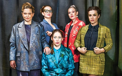 Fünf Frauen in bunten Kostümen vor einem Theatervorhang